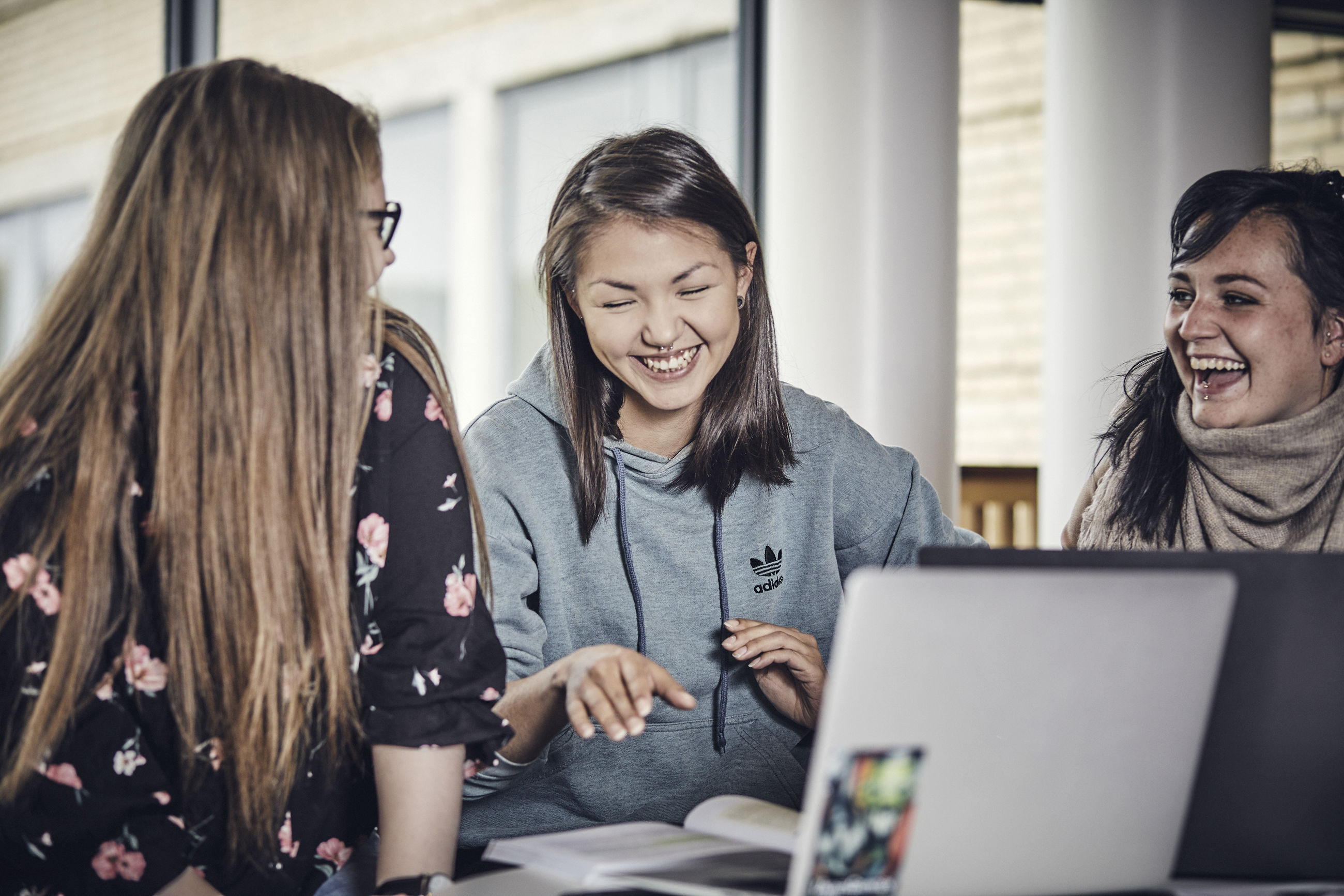 Tre unge mennesker griner, mens de snakker. De sidder med computere åbne foran sig; klar til at studere.